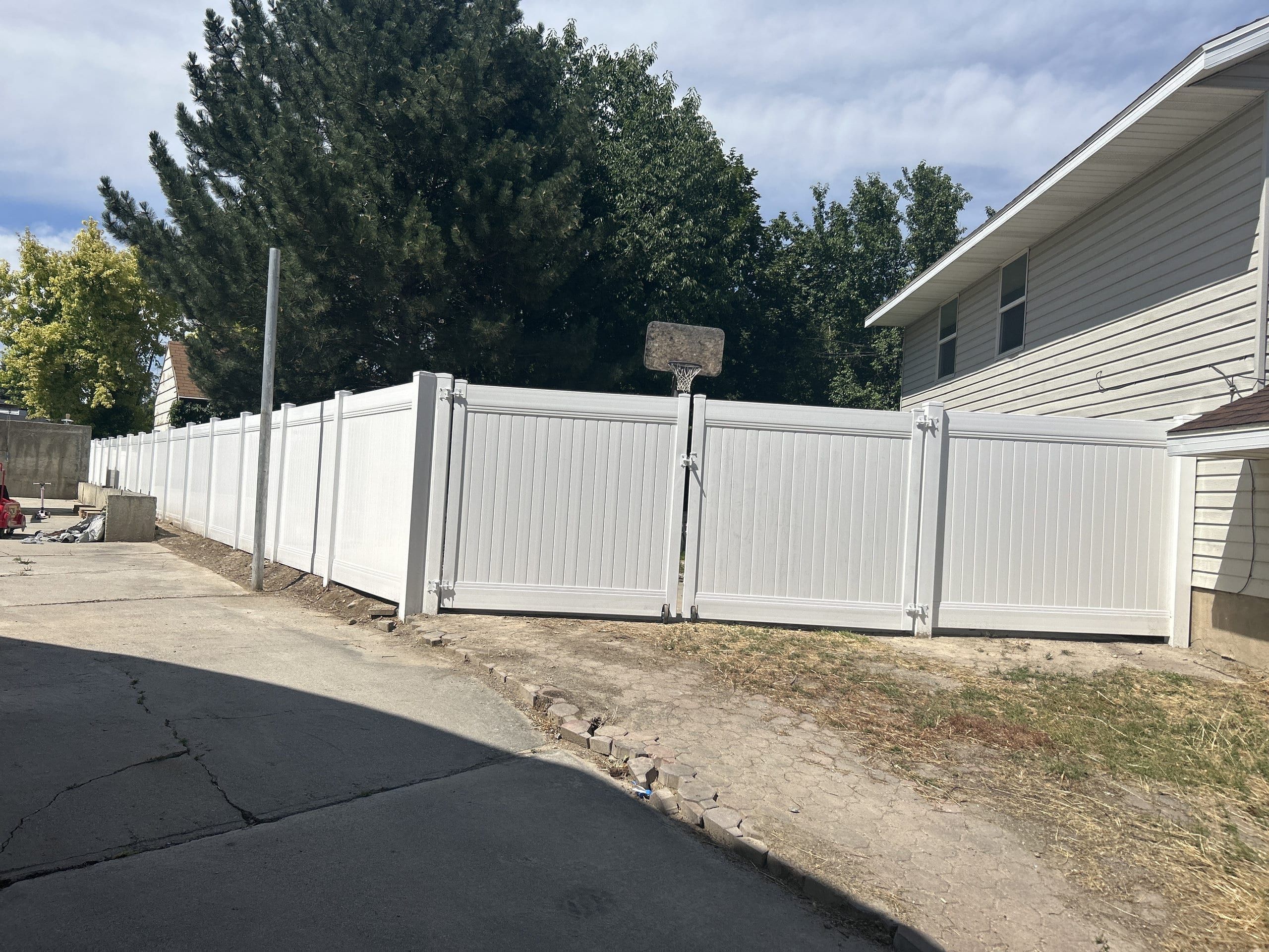 White vinyl privacy fence with a double gate beside a concrete driveway, next to a house